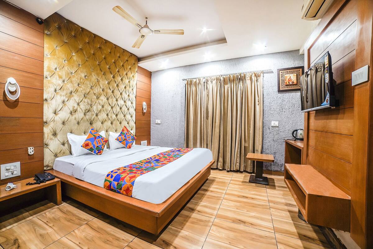 Una habitación de hotel con cabecera capitonada, cama con almohadas coloridas, ventilador de techo, televisor y suelo de madera.