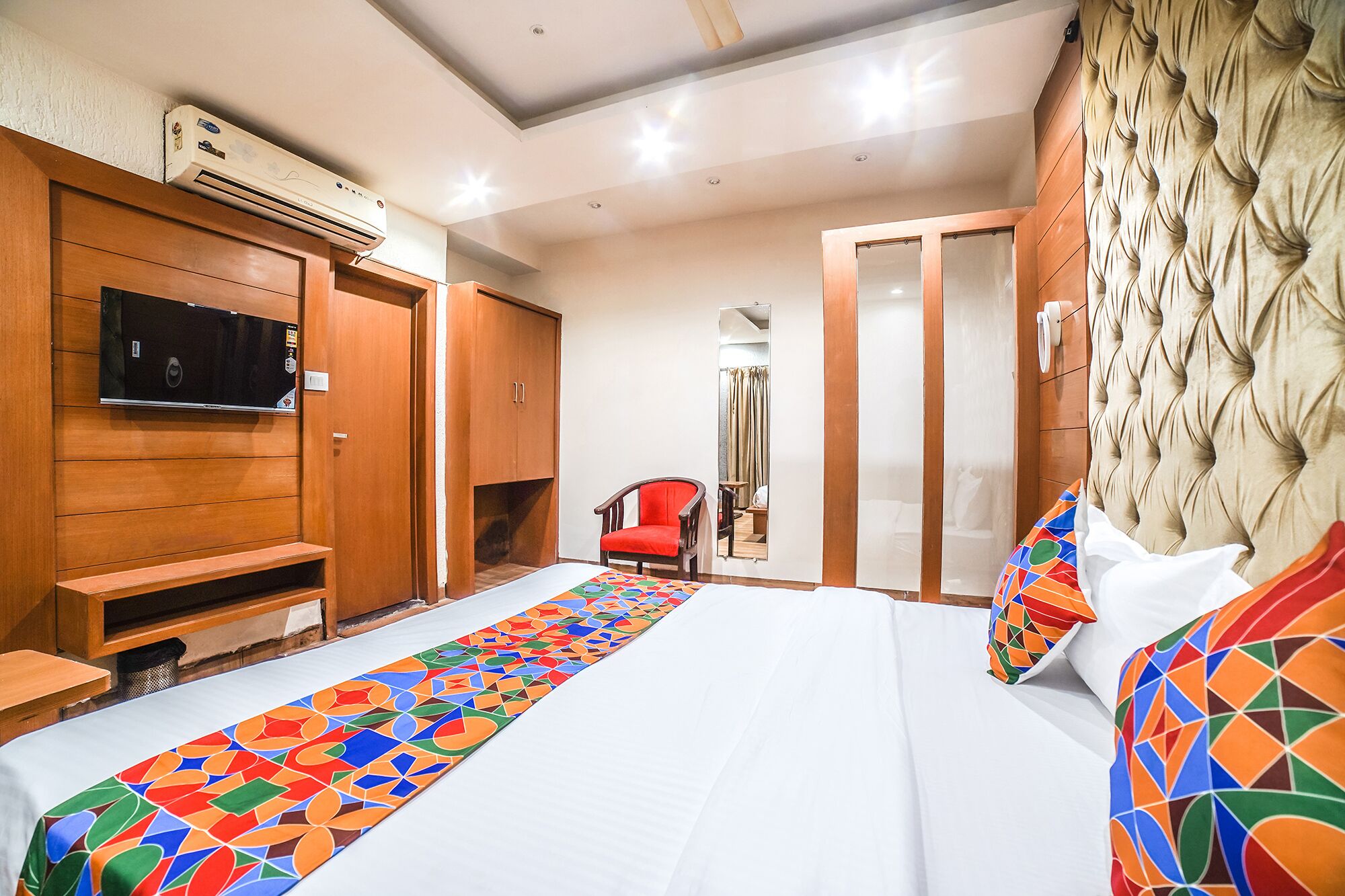A hotel room with a bed, a TV, a wardrobe, a mirror, and a chair.