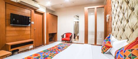 A hotel room with a bed, a TV, a wardrobe, a mirror, and a chair.