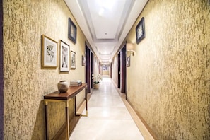 A hotel hallway with framed botanical prints on the walls, a wooden console table with a vase and books, and a potted orchid. - FabHotel Johri Regency (Bhopal)