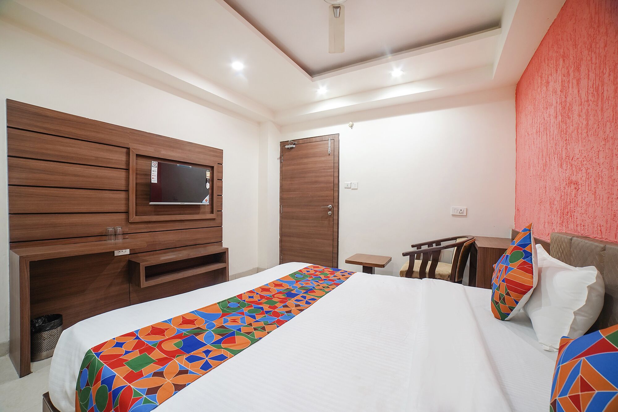 Habitación de hotel con una cama grande, un televisor instalado en un mueble de madera, una mesita pequeña y una silla.