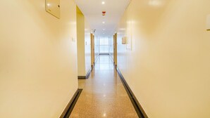 A long, narrow hallway with a polished floor, light-colored walls, and a ceiling with recessed lighting and a smoke detector. - Fabhotel Northern Suites (Bengaluru)