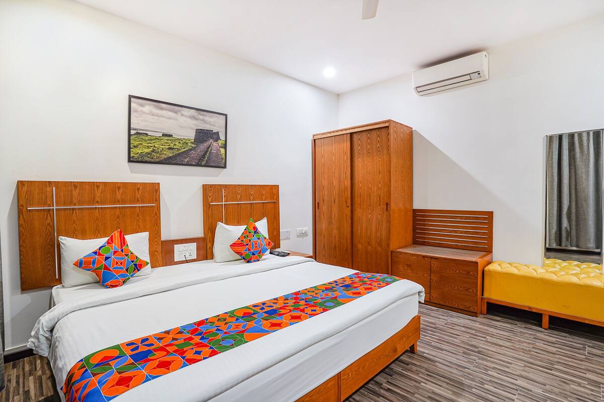 A hotel room with a large bed, wooden headboard, a bench, and a wardrobe.