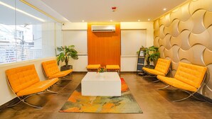 A modern waiting area with orange chairs, a white coffee table, and a wooden panel wall. - Fabhotel Northern Suites (Bengaluru)
