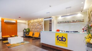 A hotel reception area with a modern design, featuring a reception desk with a logo, seating area with chairs, and a decorative wall. - Fabhotel Northern Suites (Bengaluru)