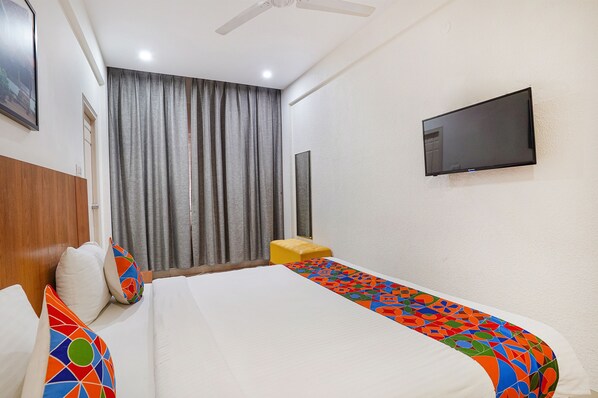 A hotel room with a bed, a TV mounted on the wall, a window with curtains, and a wooden headboard. - Fabhotel Northern Suites (Bengaluru)