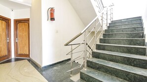 A staircase with metal railings and marble steps, leading to a landing with a fire extinguisher mounted on the wall. - Fabhotel Basera (Haridwar)