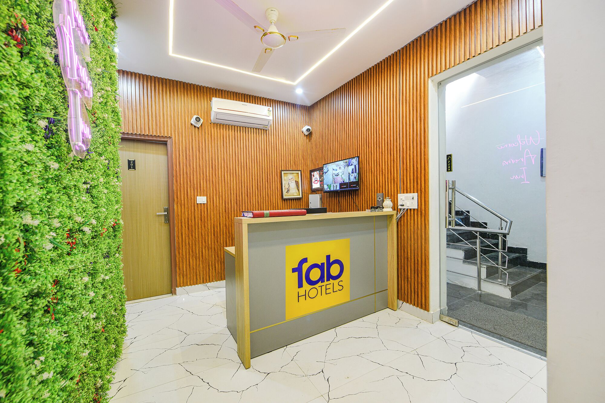 Een receptiebalie met een 'Tab Hotels' bord, een houten wand, een wand met groene planten en een trap.