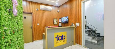 Een receptiebalie met een 'Tab Hotels' bord, een houten wand, een wand met groene planten en een trap.