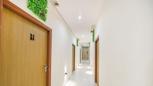 A hotel hallway with wooden doors, white walls, and a marble floor. - FabHotel Kavya Inn (Faridabad)