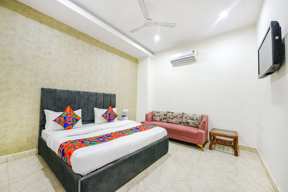 A bedroom with a bed, a sofa, a TV, and an air conditioning unit.
