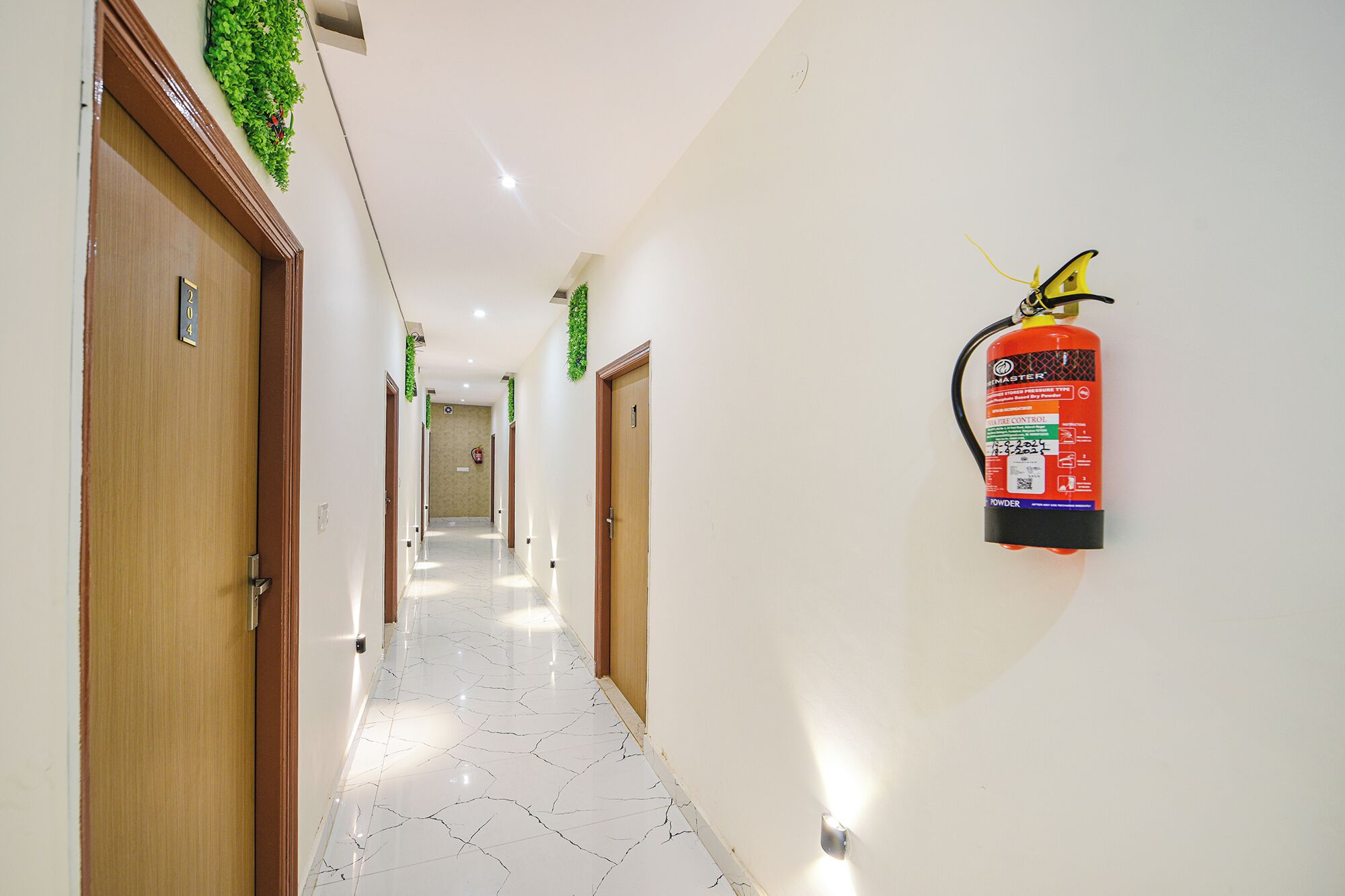 A hallway with wooden doors, a fire extinguisher mounted on the wall, and a marble floor.