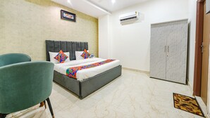 A hotel room with a bed, a chair, an air conditioning unit, and a wardrobe. - FabHotel Kavya Inn (Faridabad)