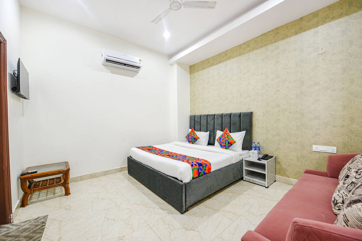 A bedroom with a bed, a nightstand, a red sofa, a ceiling fan, an air conditioner, and a small wooden table.
