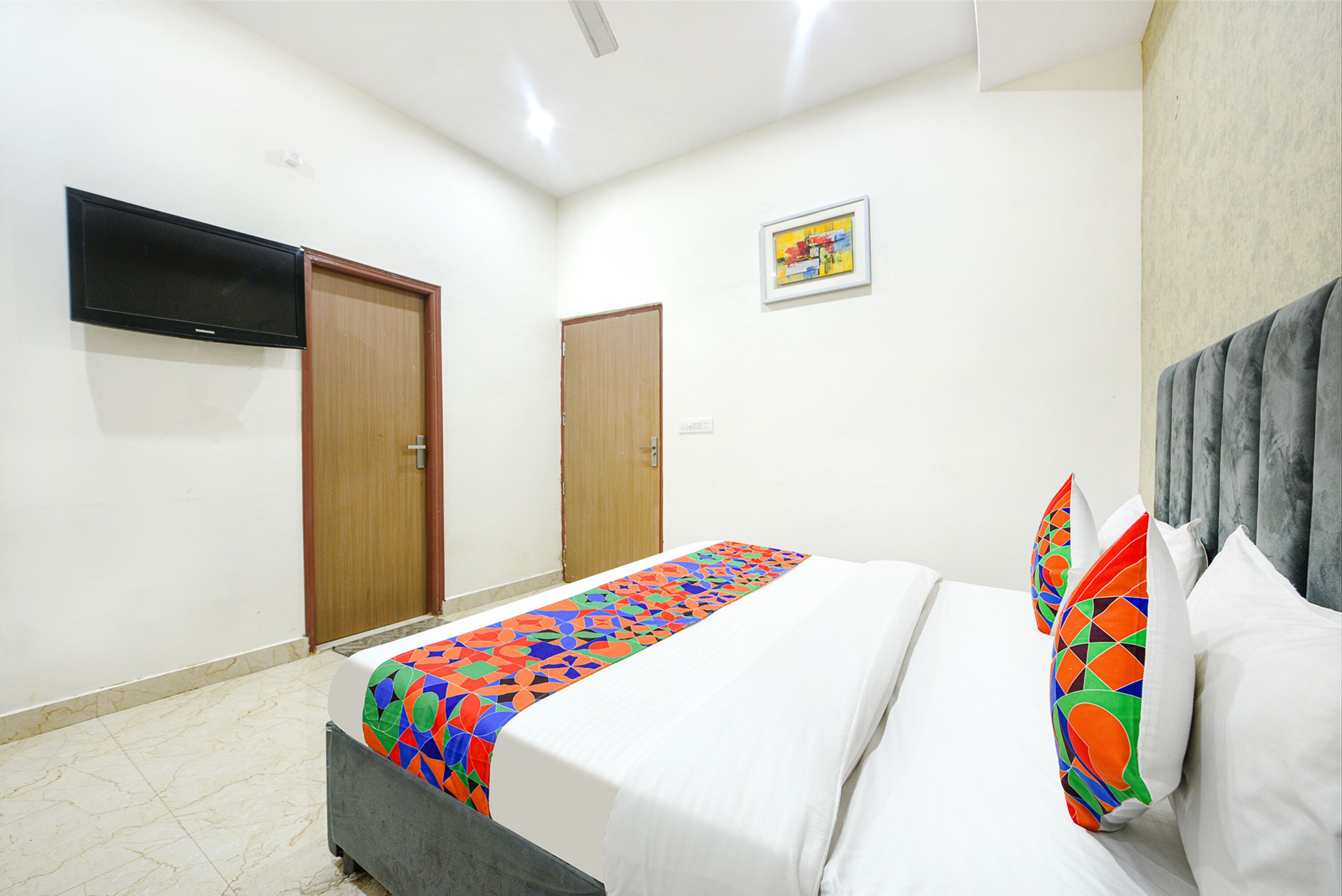 A hotel room with a bed, a television mounted on the wall, and two doors.