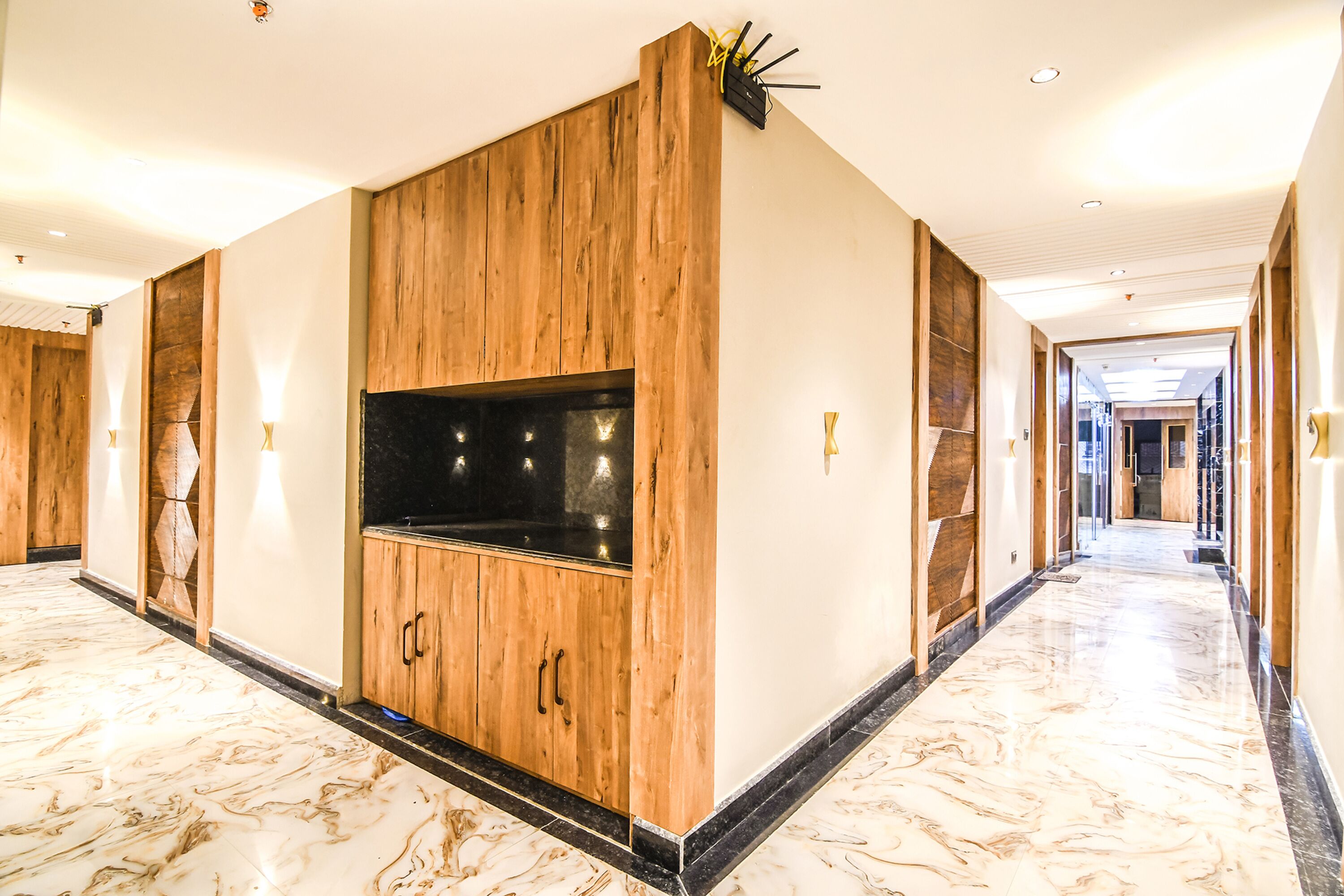 A hallway with a wooden cabinet and a black TV screen, marble flooring, and recessed lighting.