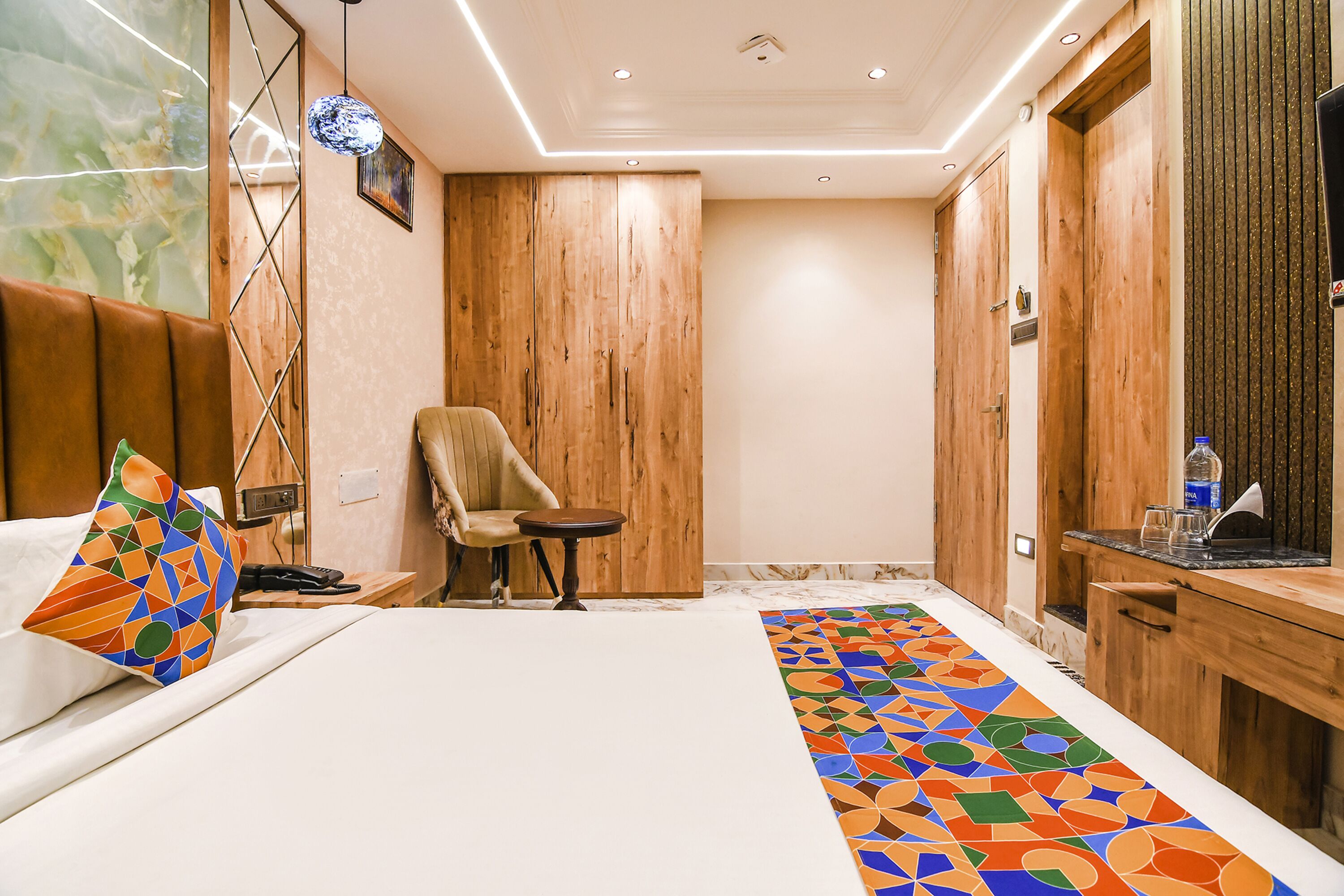 Een hotelkamer met een bed, een stoel, een klein tafeltje en een houten garderobe.