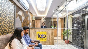 Zona de recepción con un letrero de 'fab hotels', una recepcionista y un área de estar con dos personas.