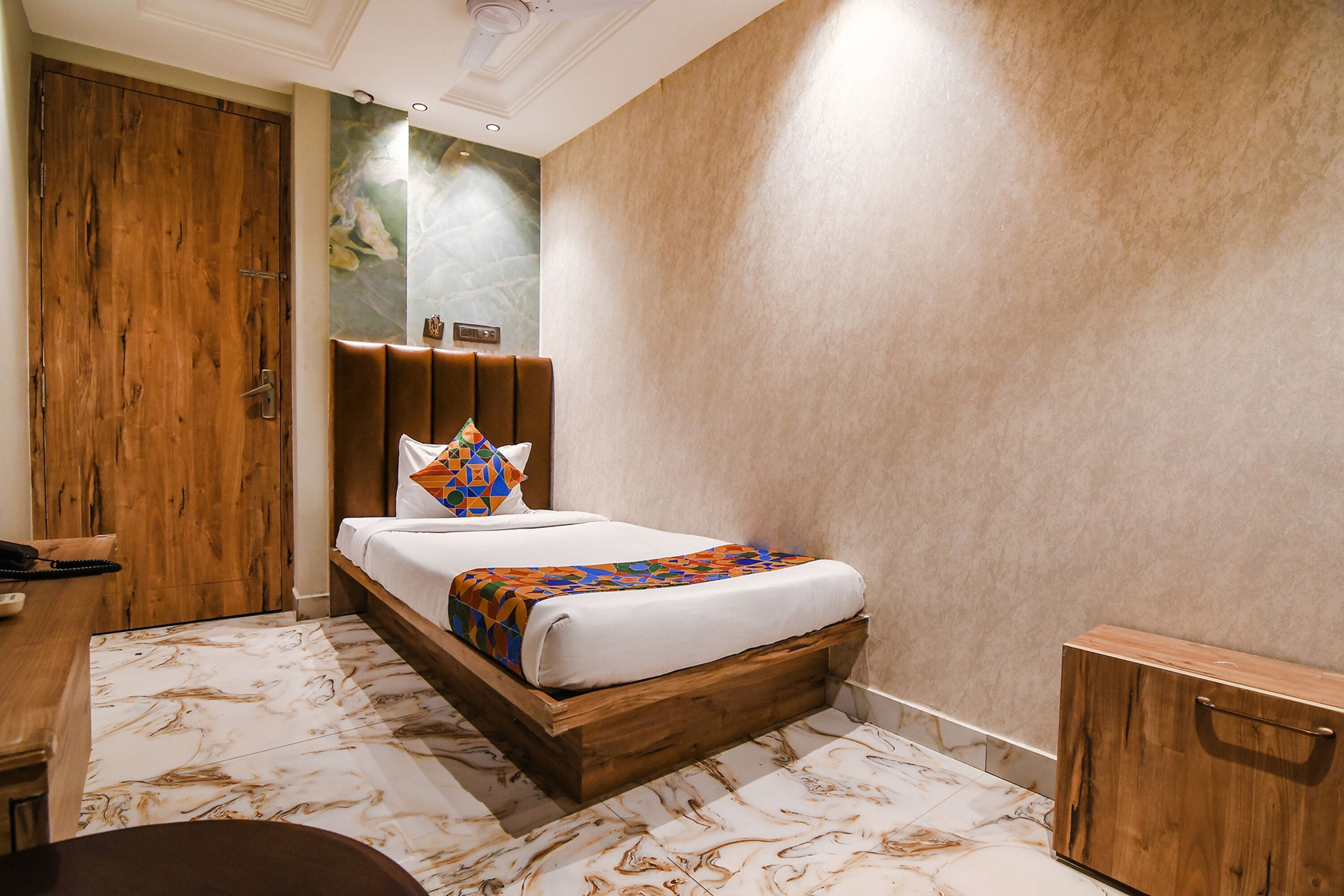 A hotel room with a wooden bed, a marble-patterned floor, a wooden wardrobe, and a wall-mounted clock.