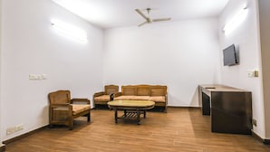 A room with a ceiling fan, a sofa, two armchairs, a small table, and a TV mounted on the wall. - Fabhotel Sunrise Villa (New Delhi)