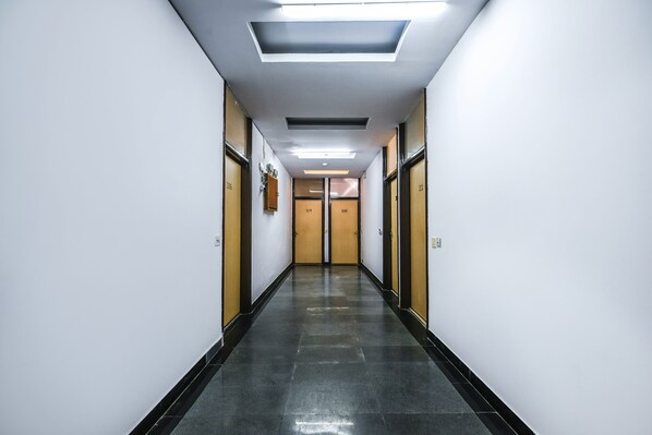 A long, narrow hallway with doors on both sides, a tiled floor, and recessed lighting on the ceiling. - Fabhotel Sunrise Villa (New Delhi)