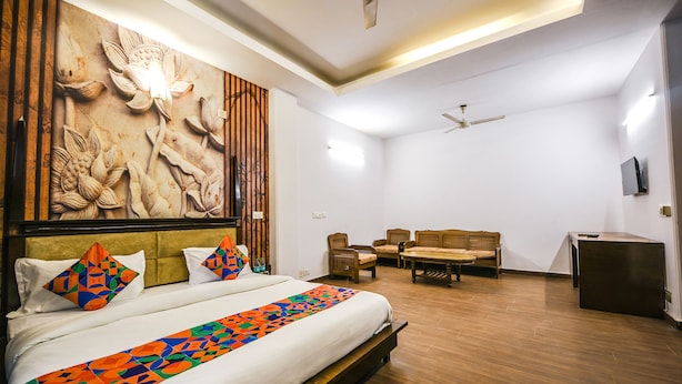 A hotel room with a large bed, a wooden headboard, a wall mural, a sofa set, and a ceiling fan. - Fabhotel Sunrise Villa (New Delhi)
