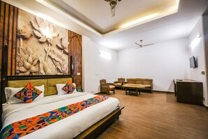 A hotel room with a large bed, a wooden headboard, a wall mural, a sofa set, and a ceiling fan. - Fabhotel Sunrise Villa (New Delhi)