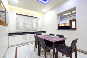 A modern kitchen with white cabinets, a black countertop, and a patterned backsplash. There is a dining table with six chairs and a purple table runner. - Fabhotel De Alphabet Ii (Hyderabad)