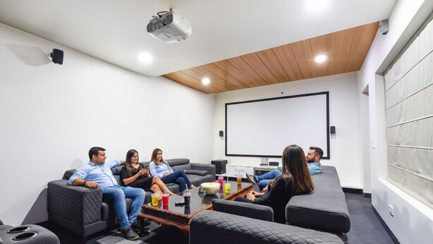A modern home theater room with a large screen, comfortable seating, and a projector. - Fabhotel De Alphabet Ii (Hyderabad)