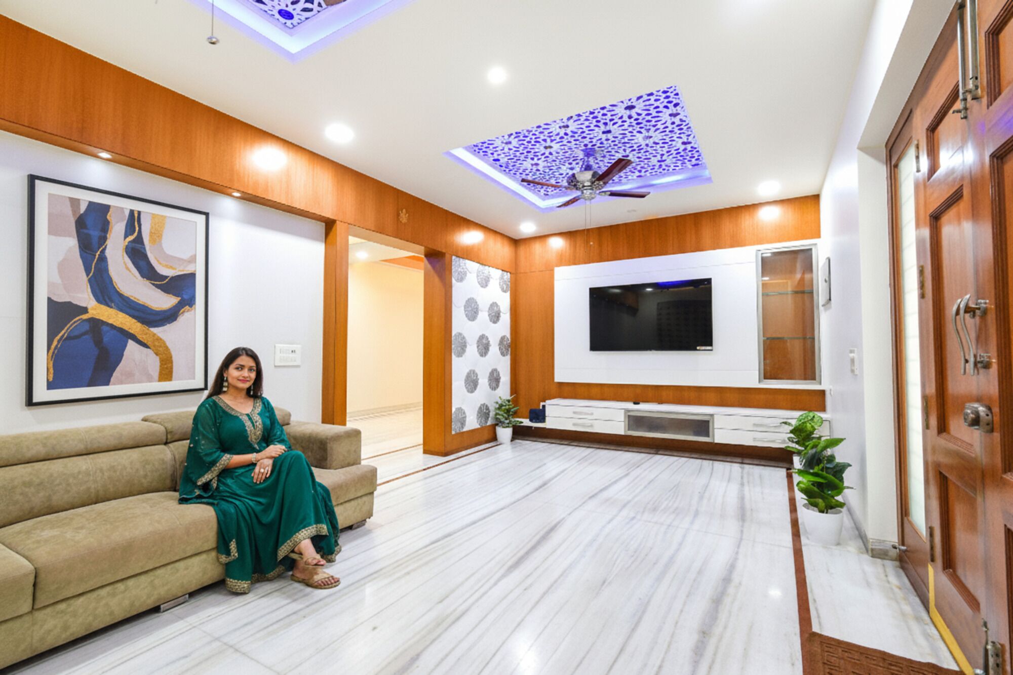 A modern living room with a sofa, a flat-screen TV mounted on the wall, and a ceiling fan.