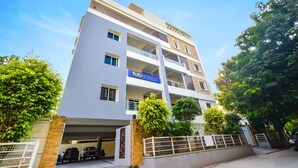 A multi-story hotel with a modern design, featuring balconies, a parking garage, and lush greenery. - Fabhotel De Alphabet Ii (Hyderabad)