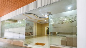 Un hall d’hôtel moderne avec des portes en verre, un plafond en bois et un espace salon visible à travers le verre.