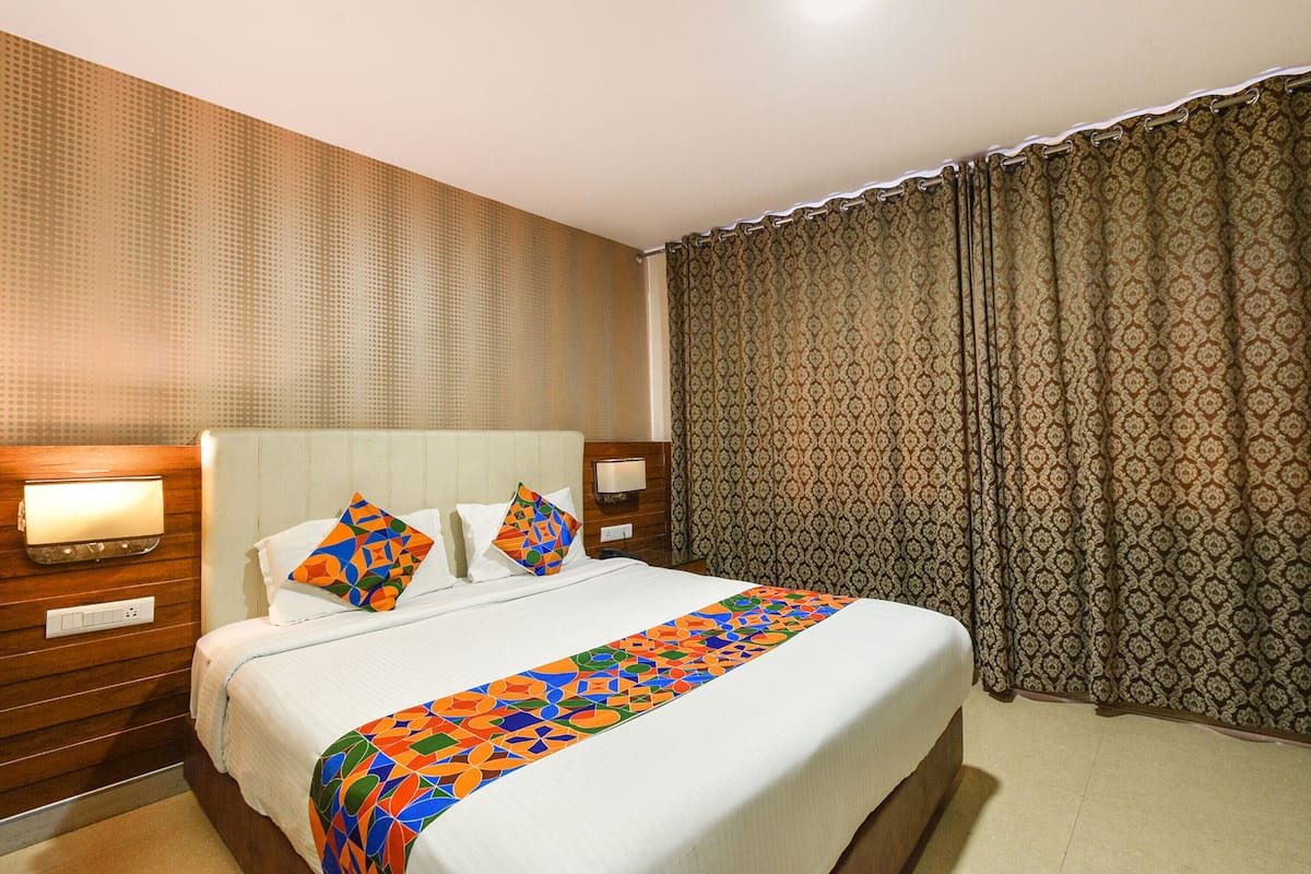 A hotel room with a large bed, a patterned curtain, and a wall-mounted light.