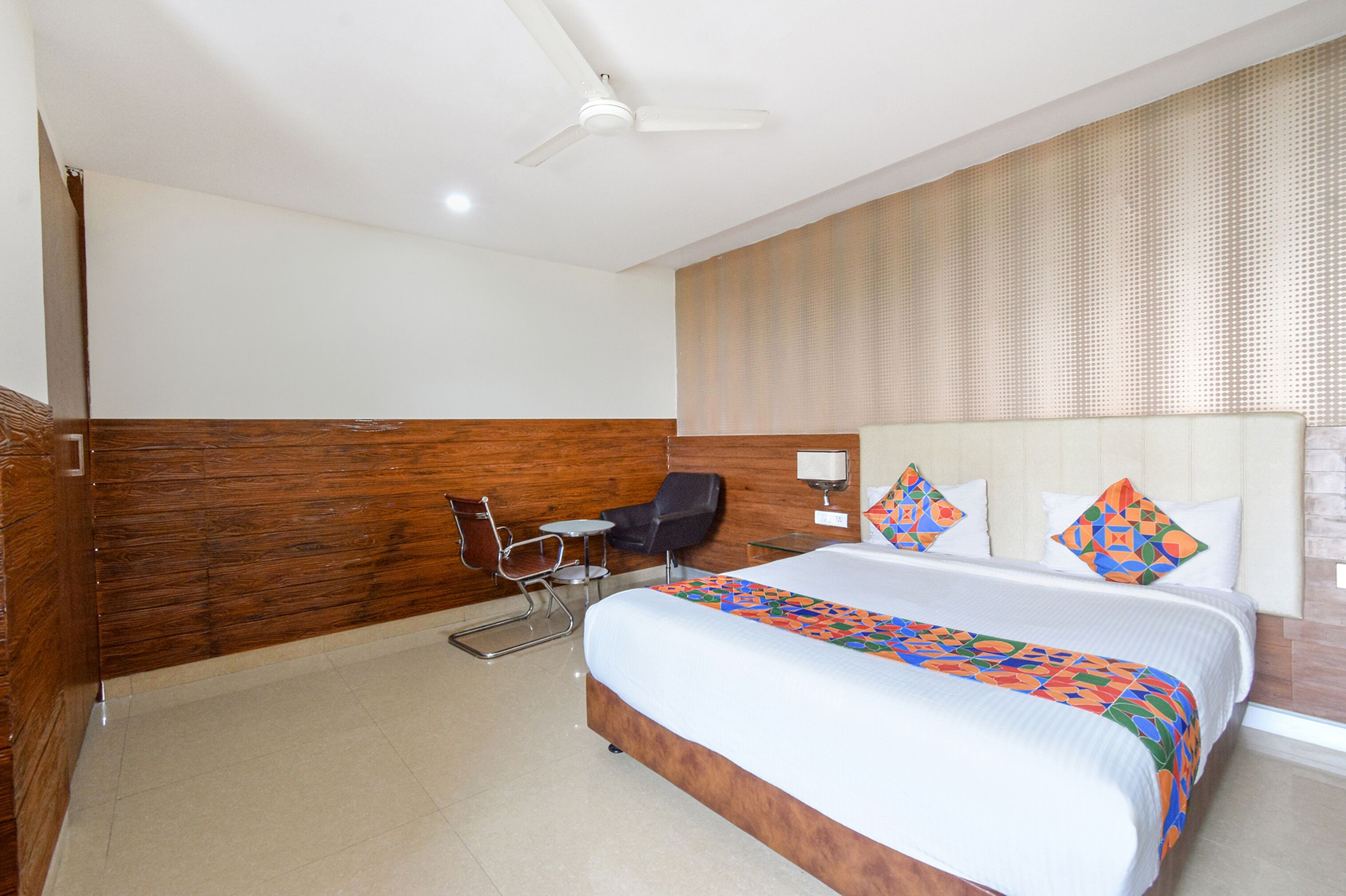 A hotel room with a large bed, a desk, a chair, and a ceiling fan.
