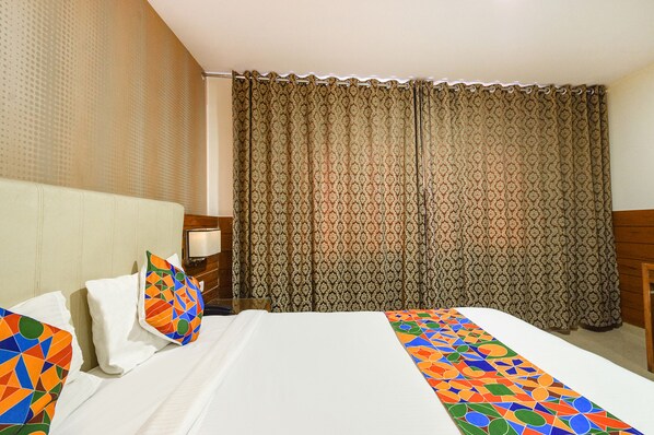 A hotel room with a bed, pillows, a nightstand, and curtains. - Oriva Millennium Grand (Hyderabad)