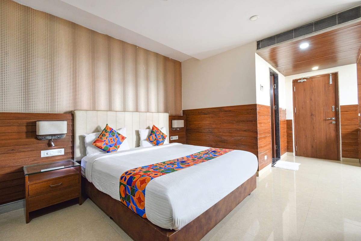 A hotel room with a large bed, wooden headboard, and a nightstand with a lamp.