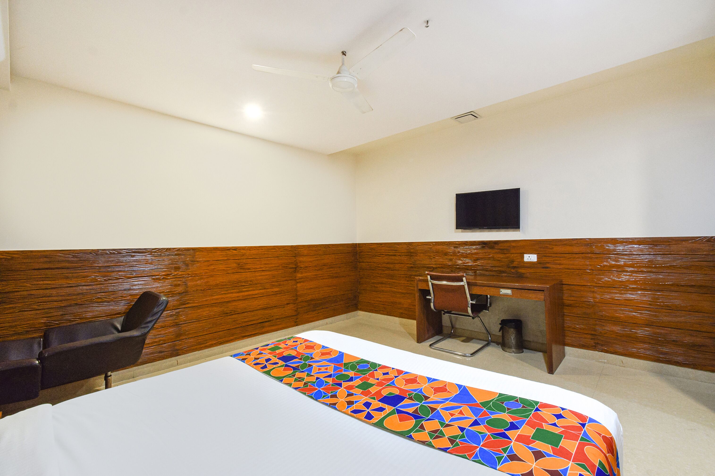 A hotel room with a bed, a desk, a chair, and a ceiling fan.
