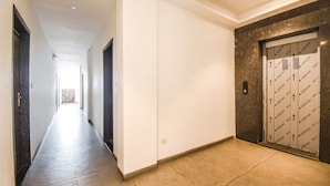 A hallway with a tiled floor, a white wall, and a door with a patterned design. - Fabhotel Seven Seas (Pune)