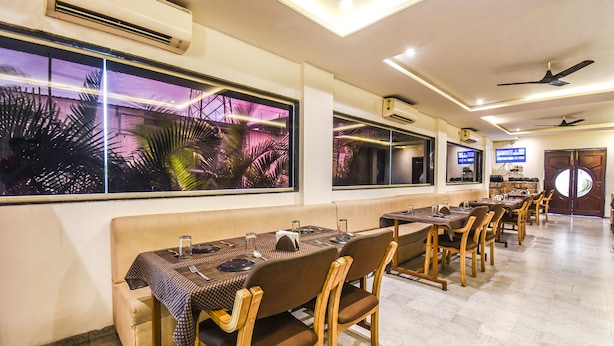 A restaurant with long tables, wooden chairs, and large windows with tropical views. - Fabhotel Seven Seas (Pune)