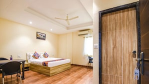 A hotel room with a wooden floor, a bed with colorful pillows, a desk with a chair, and a ceiling fan. - Fabhotel Seven Seas (Pune)