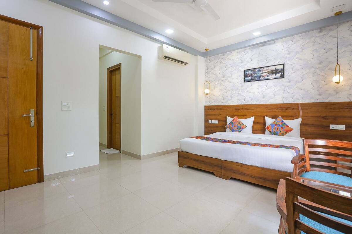 Een hotelkamer met een houten bed, een houten stoel, een plafondventilator en een aan de muur bevestigde airconditioner.