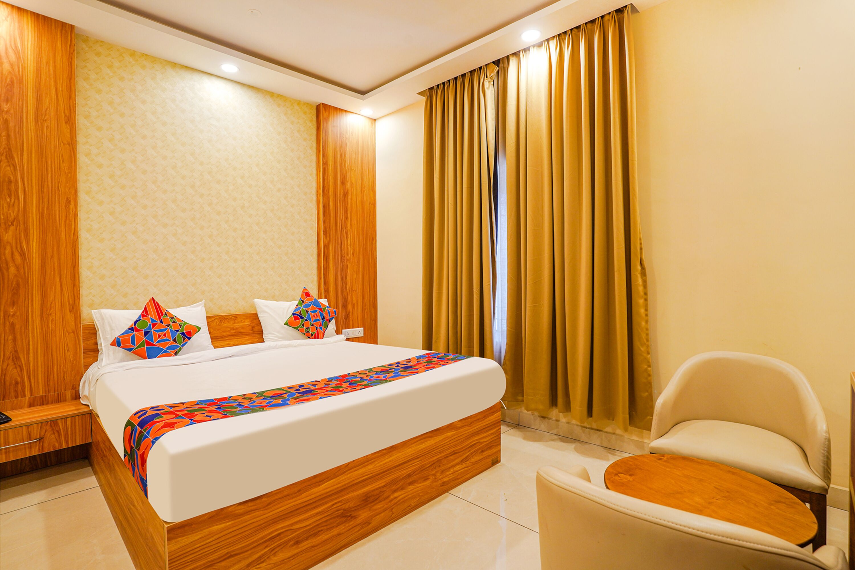 A modern hotel room with a large bed, a wooden headboard, a white armchair, and a window with curtains.