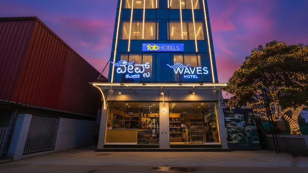 Un hôtel doté d’une façade moderne, d’une enseigne indiquant « fabHOTELS » et « WAVES HOTEL », et d’une vitrine bien visible où sont exposés divers articles.