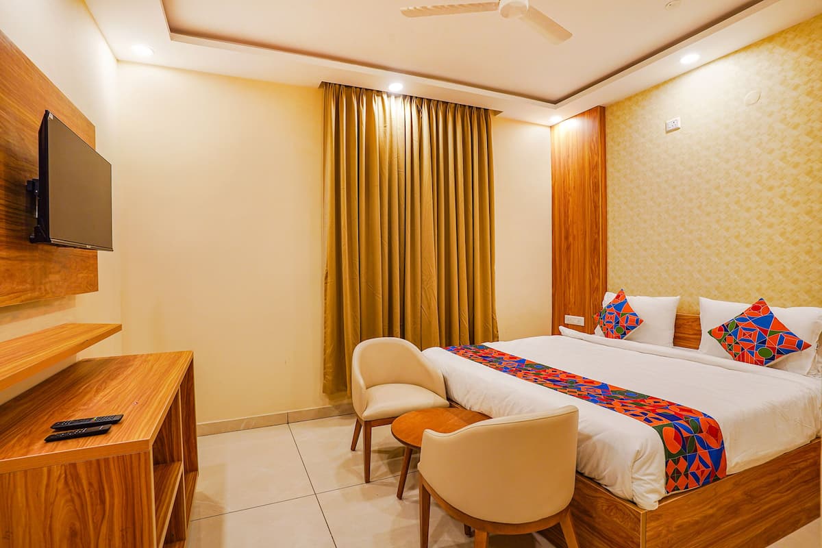 A hotel room with a bed, a desk, a chair, a television, and a window with curtains.