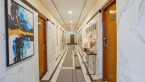 Un couloir d’hôtel aux murs de marbre, orné de tableaux encadrés et doté d’un sol recouvert de moquette.