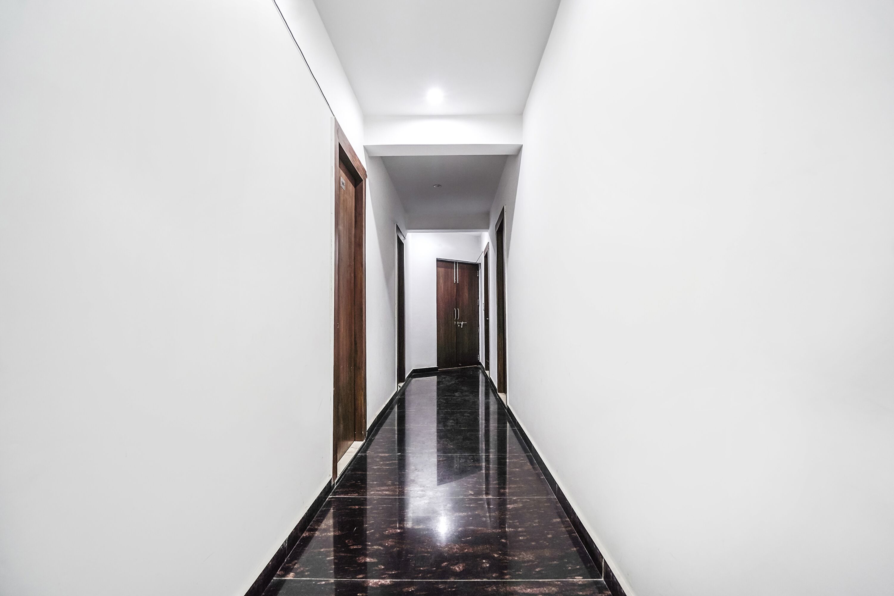 Un corridoio stretto e lucido, con pareti bianche e pavimento scuro, che conduce a una porta in fondo.