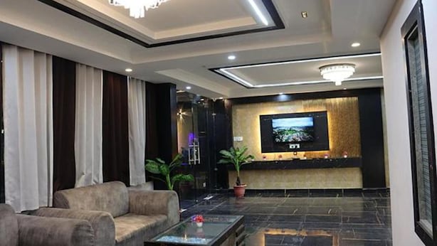 A modern lobby with a sofa, a coffee table, a TV mounted on the wall, and a chandelier. - Fabhotel Sky Heights (Haridwar)