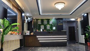 A modern reception area with a marble floor, a wooden reception desk, and a green wall with plants. - Fabhotel Sky Heights (Haridwar)