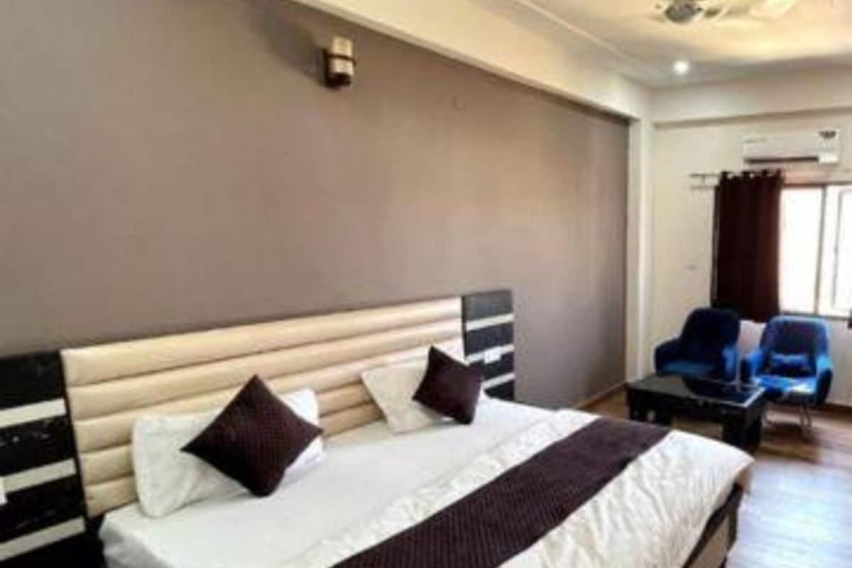 A hotel room with a large bed, a headboard, a nightstand, and a seating area with chairs.