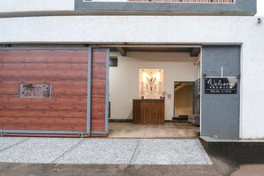L’entrée d’un hôtel, avec une porte en bois, un comptoir d’accueil et une pancarte indiquant : « Bienvenue, emplacement de choix n° L-12/24 ».